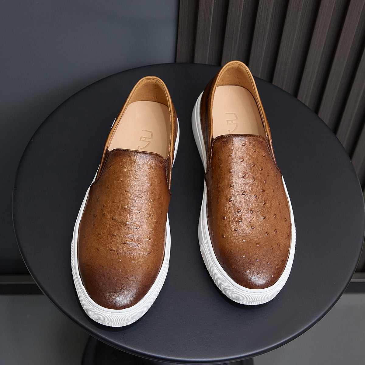 Pair of brown leather slip-on sneakers with perforations, tan lining, and white sole