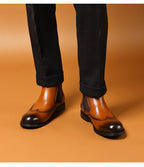Men's brown leather chelsea dress boots worn with dark pants, polished wingtip-style toe.