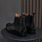 Back view of men's pointed-toe black chelsea boots with pull tabs and stacked heel