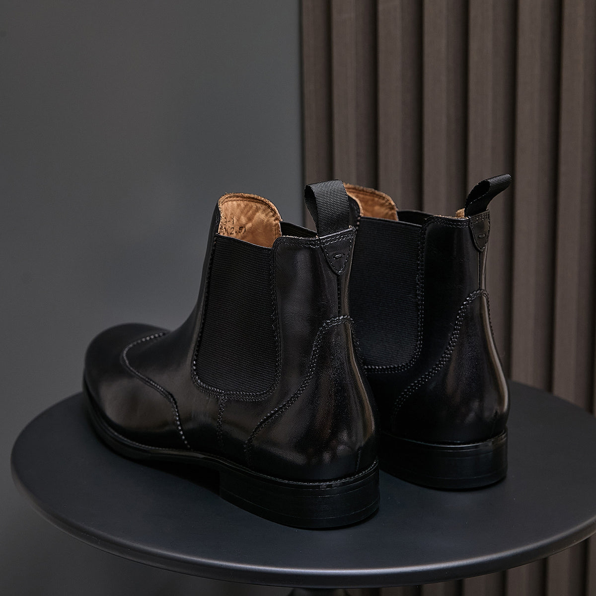 Back view of men's pointed-toe black chelsea boots with pull tabs and stacked heel