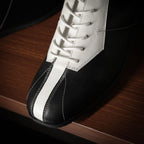 Close-up of black and white leather sneaker with white laces and stitched stripe panel.