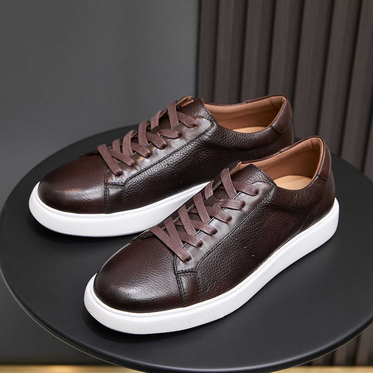 Pair of dark brown leather lace-up sneakers on display with white soles
