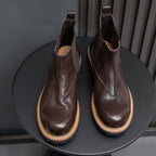 Pair of dark brown suede Chelsea boots with elastic side panels and tan rubber sole