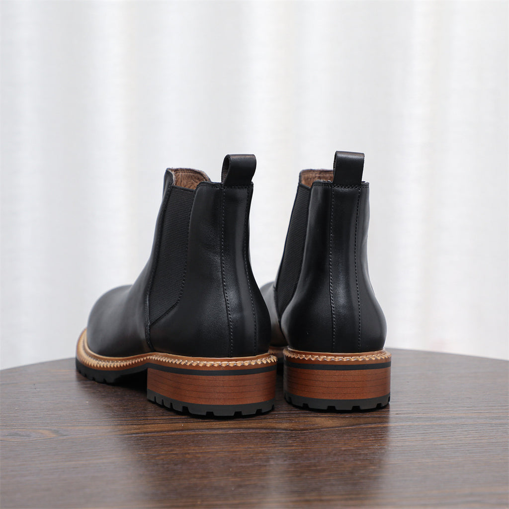 Pair of black pointed-toe Chelsea boots showing back pull tabs and lug sole