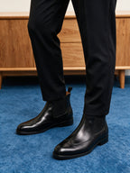 Black pointed-toe chelsea boots worn with dark pants, elastic side panels visible