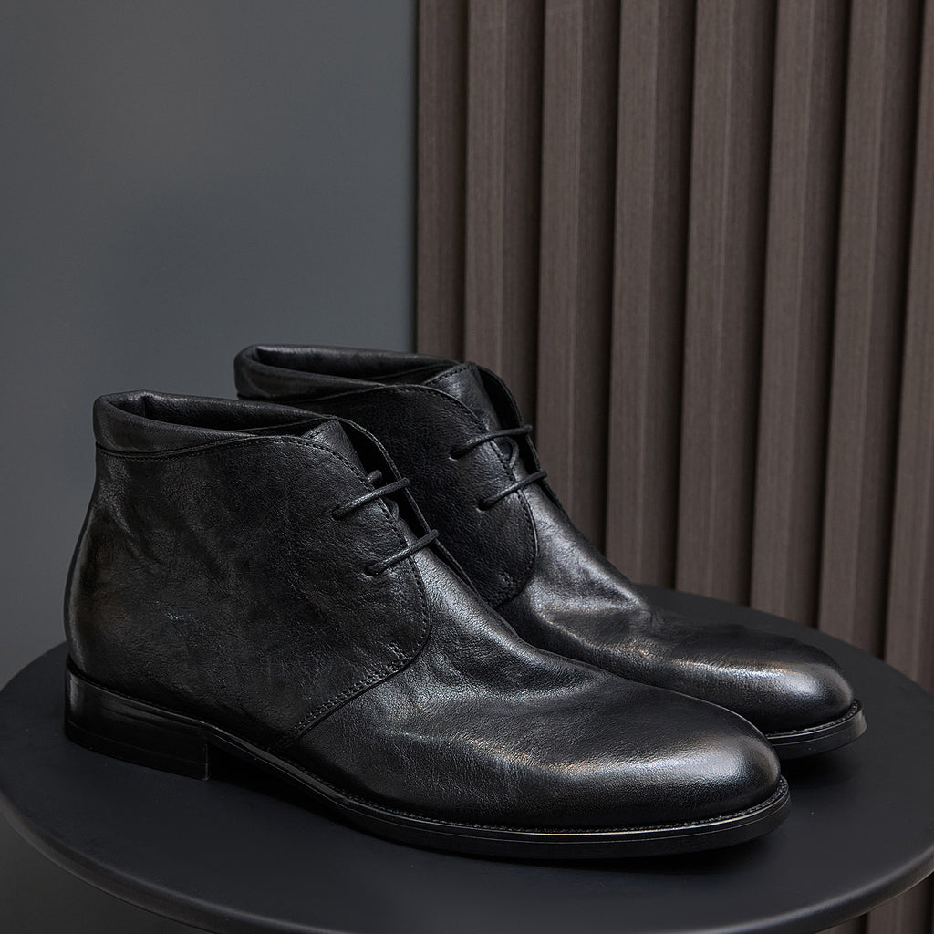 Black leather lace-up chukka boots, side view with eyelets and stitched seam.