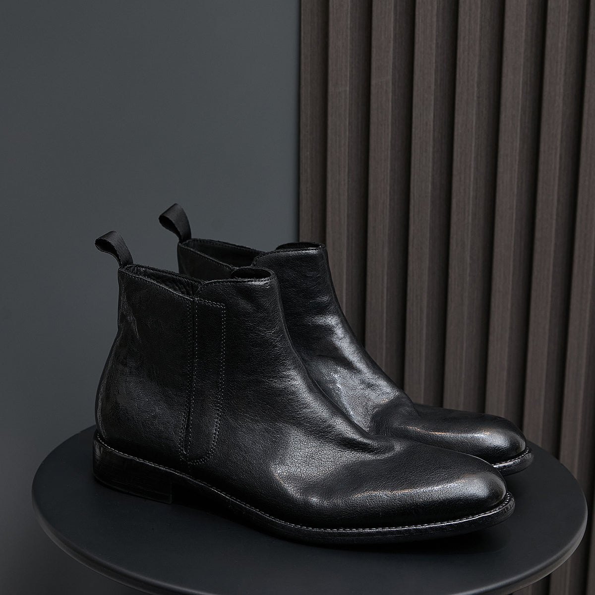 Black leather pointed-toe side-zip boots on a tray with stitched welt