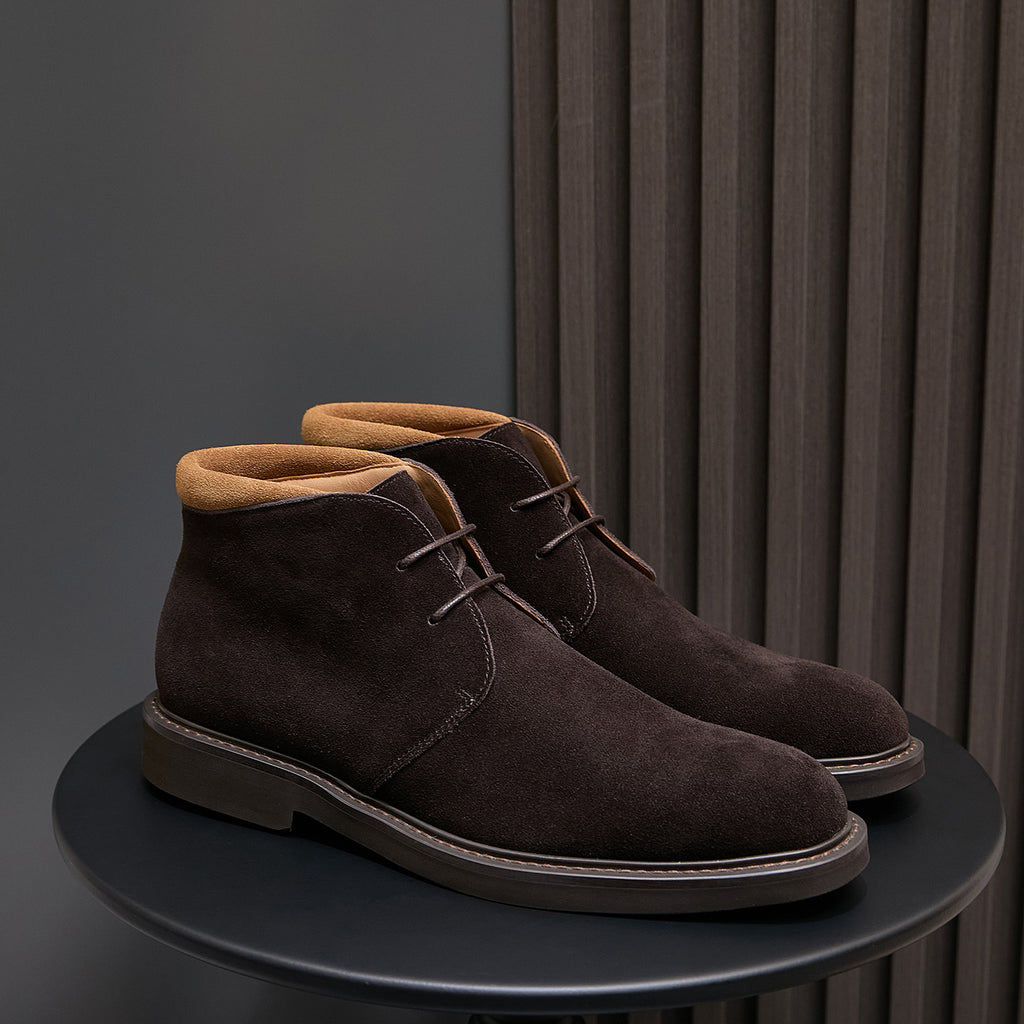 Pair of men's dark brown suede lace-up chukka boots on a round display stand