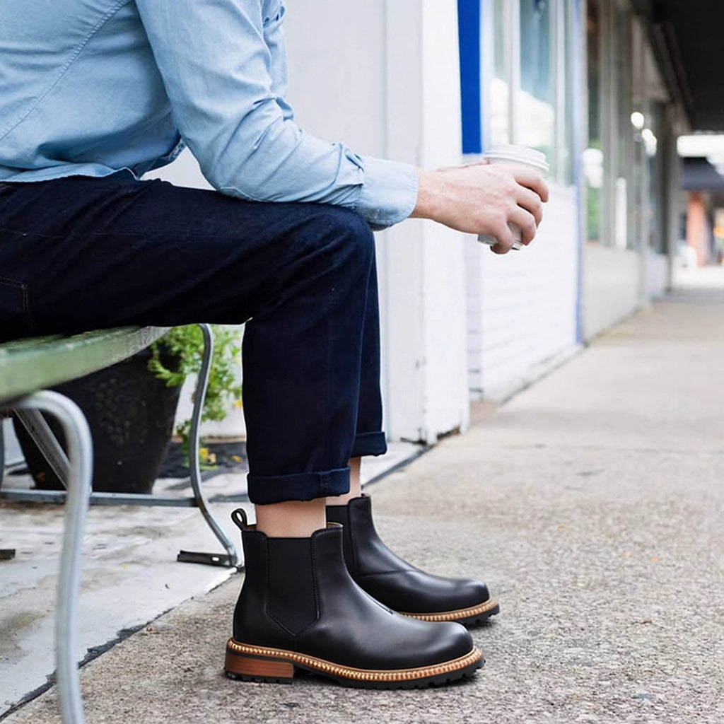 Men's black pointed-toe Chelsea dress boots worn with dark pants, rugged tread outsole