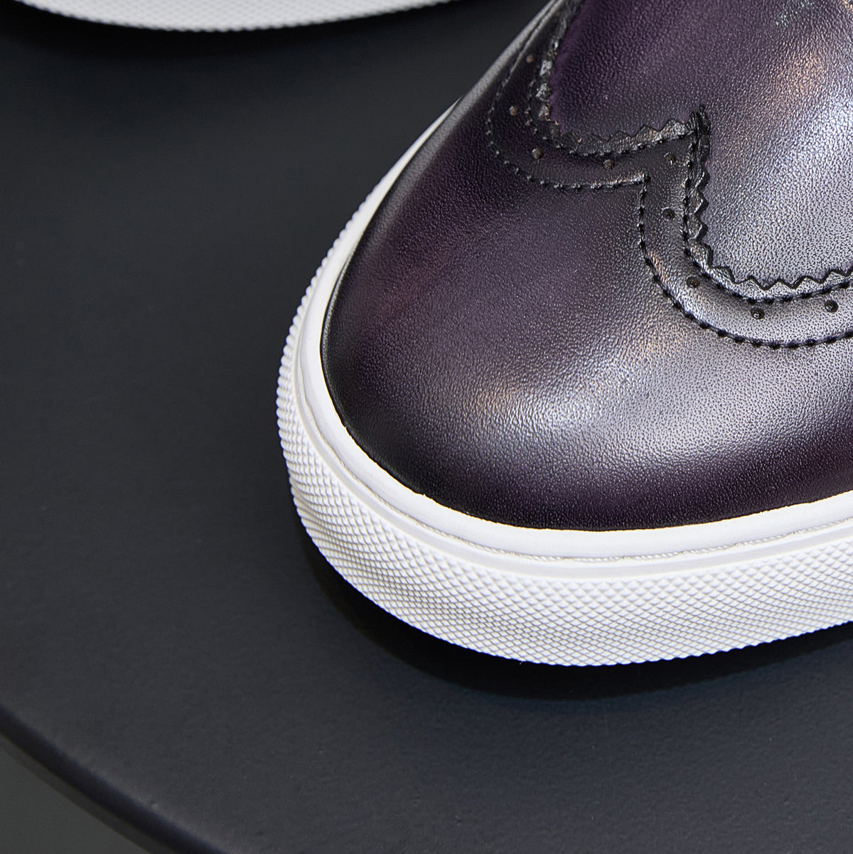 Dark purple leather sneaker toe with stitched seam and textured white sole