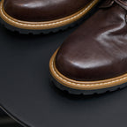 Dark brown leather boot toe with tan welt stitching and textured rubber outsole