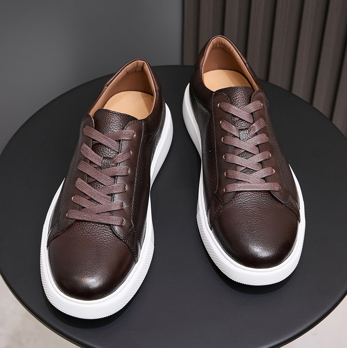 Dark brown leather lace-up sneakers with white midsoles, pair on stand