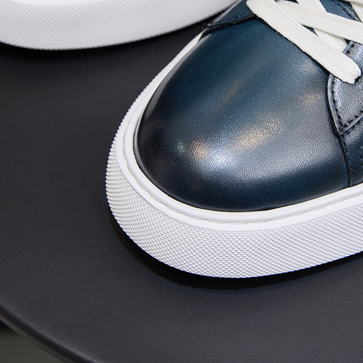 Close-up of blue leather sneaker toe with white laces and textured sole