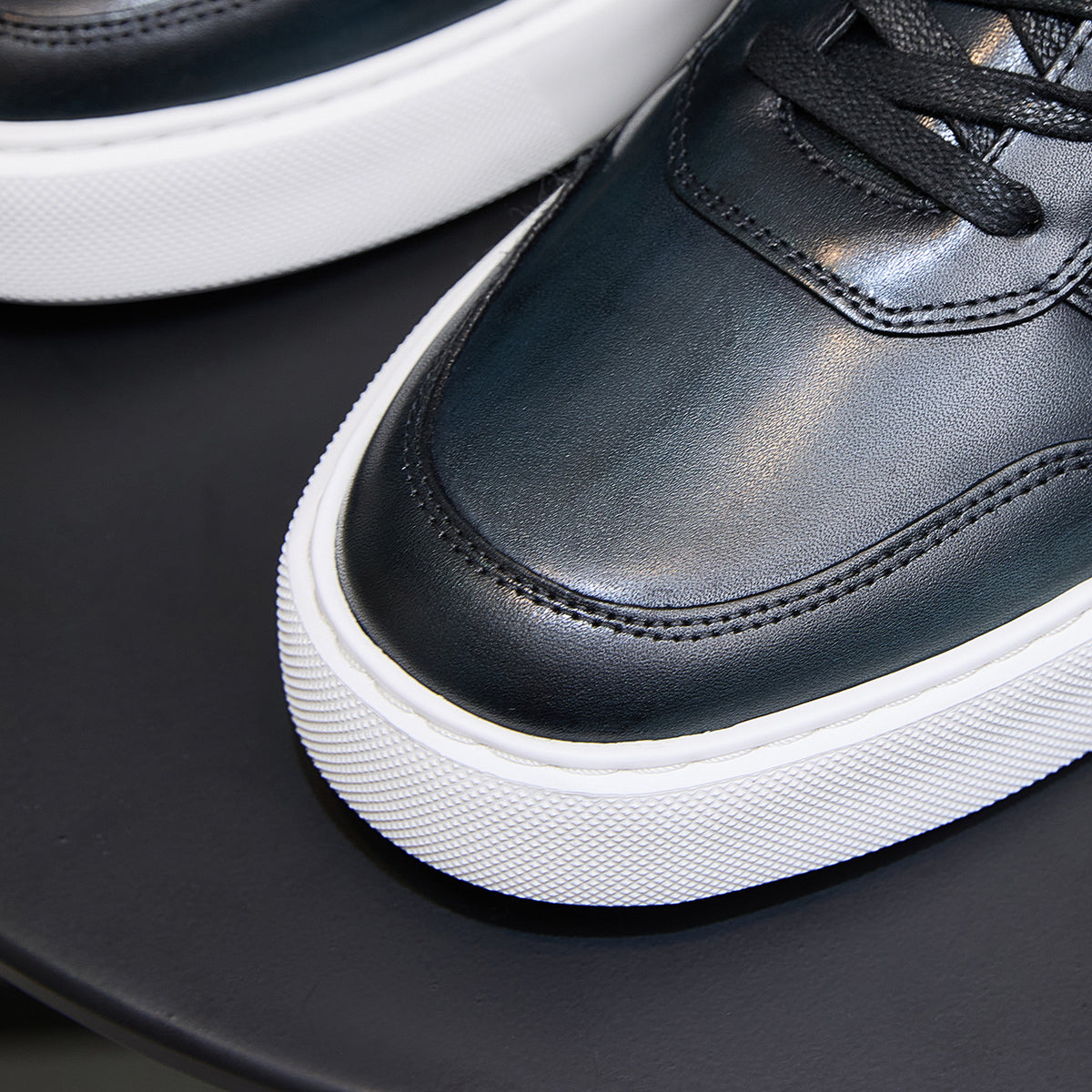 Dark blue leather sneaker toe and lace area with stitched seams, white platform sole.