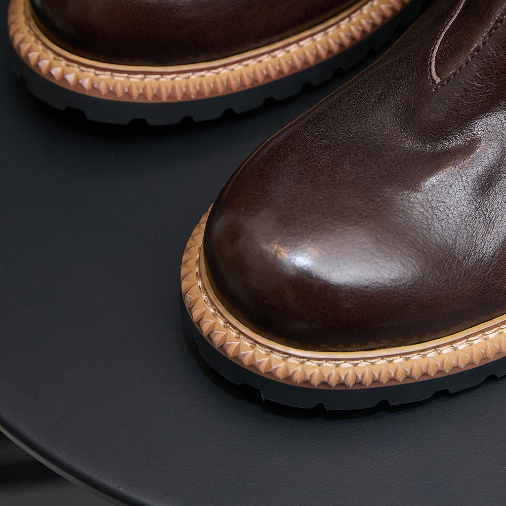 Close-up of dark brown suede Chelsea boot with tan welt trim and textured rubber sole