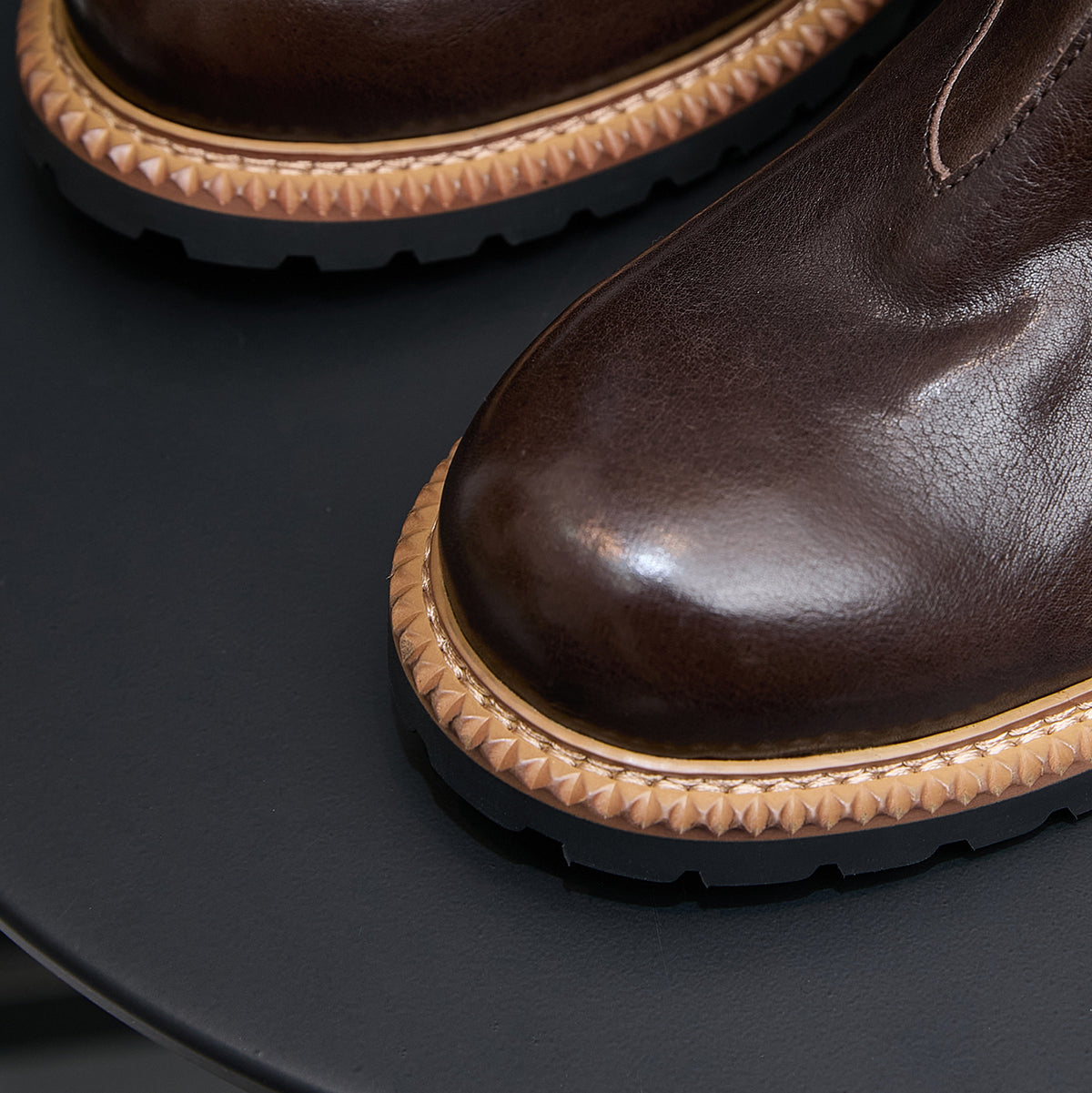Close-up of dark brown suede Chelsea boot with tan welt trim and textured rubber sole