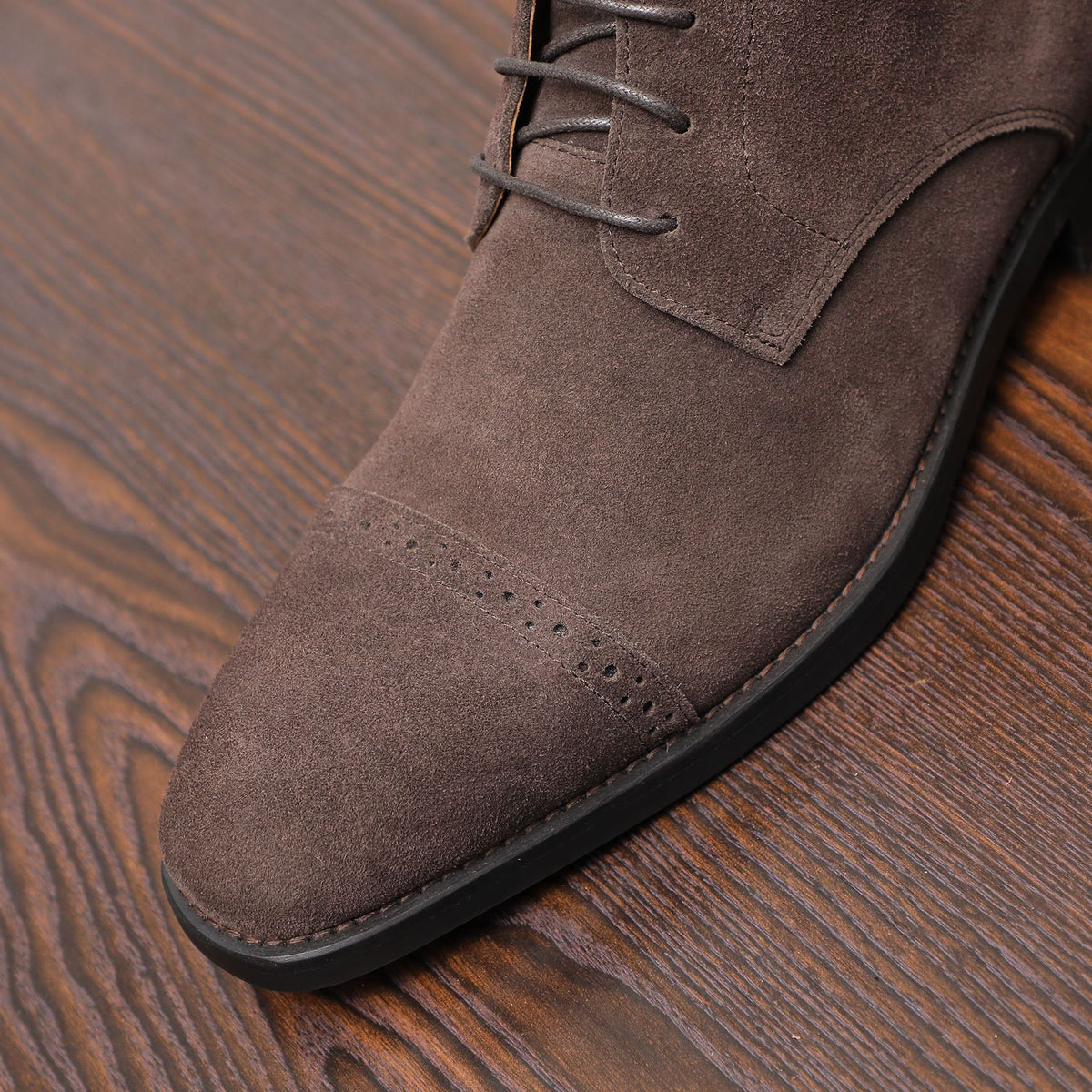 Dark brown lace-up chukka boot toe with perforations and black rubber sole