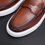 Men's brown leather moc-toe slip-on sneaker close-up with contrast stitching and strap.