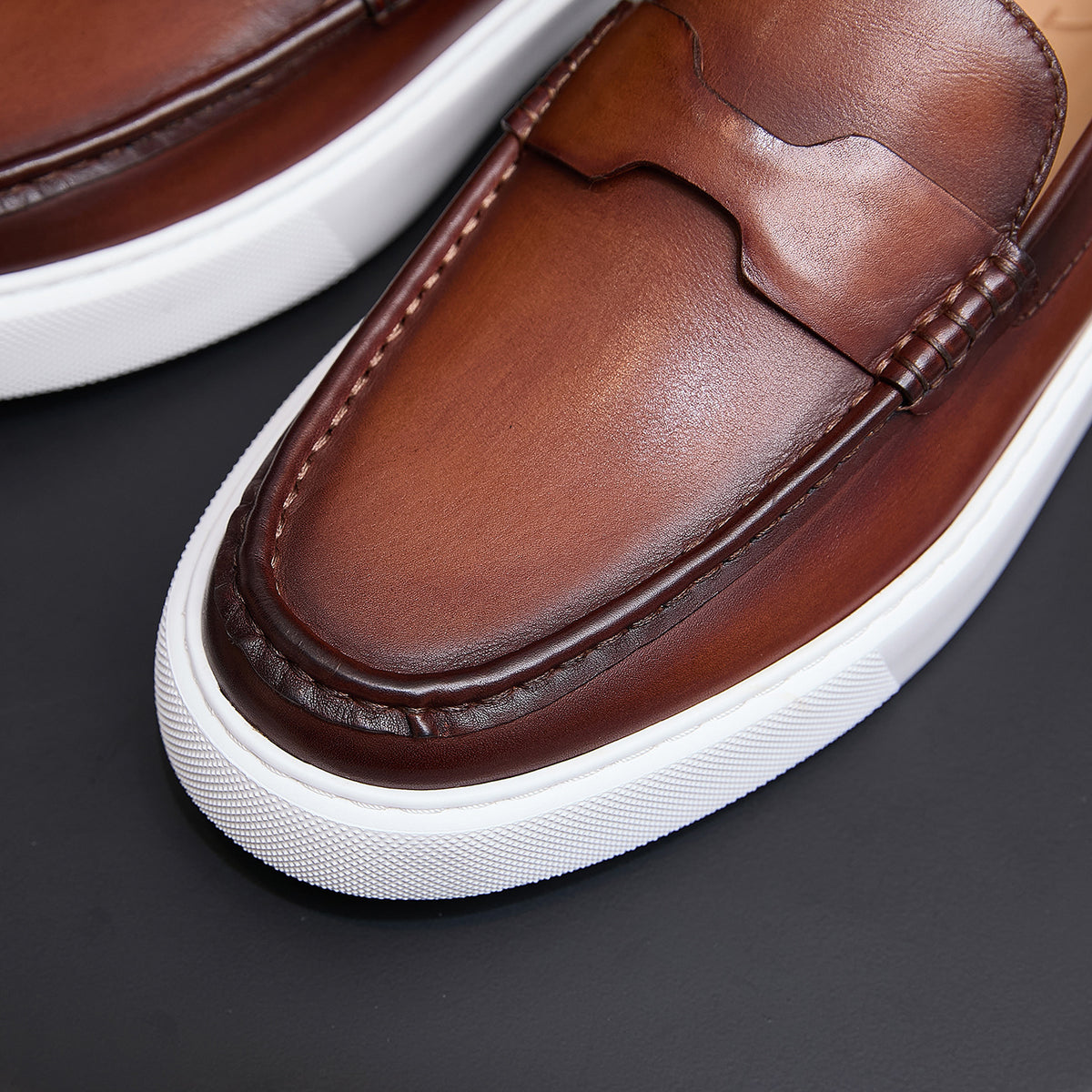 Men's brown leather moc-toe slip-on sneaker close-up with contrast stitching and strap.