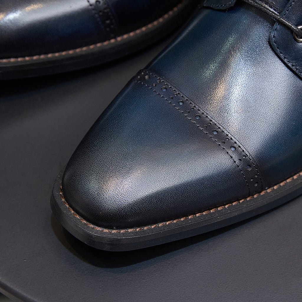 Leather boot toe close-up with brogue perforations and tan welt, dark blue.