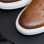 Close-up of brown leather slip-on sneaker upper with perforations and white sole