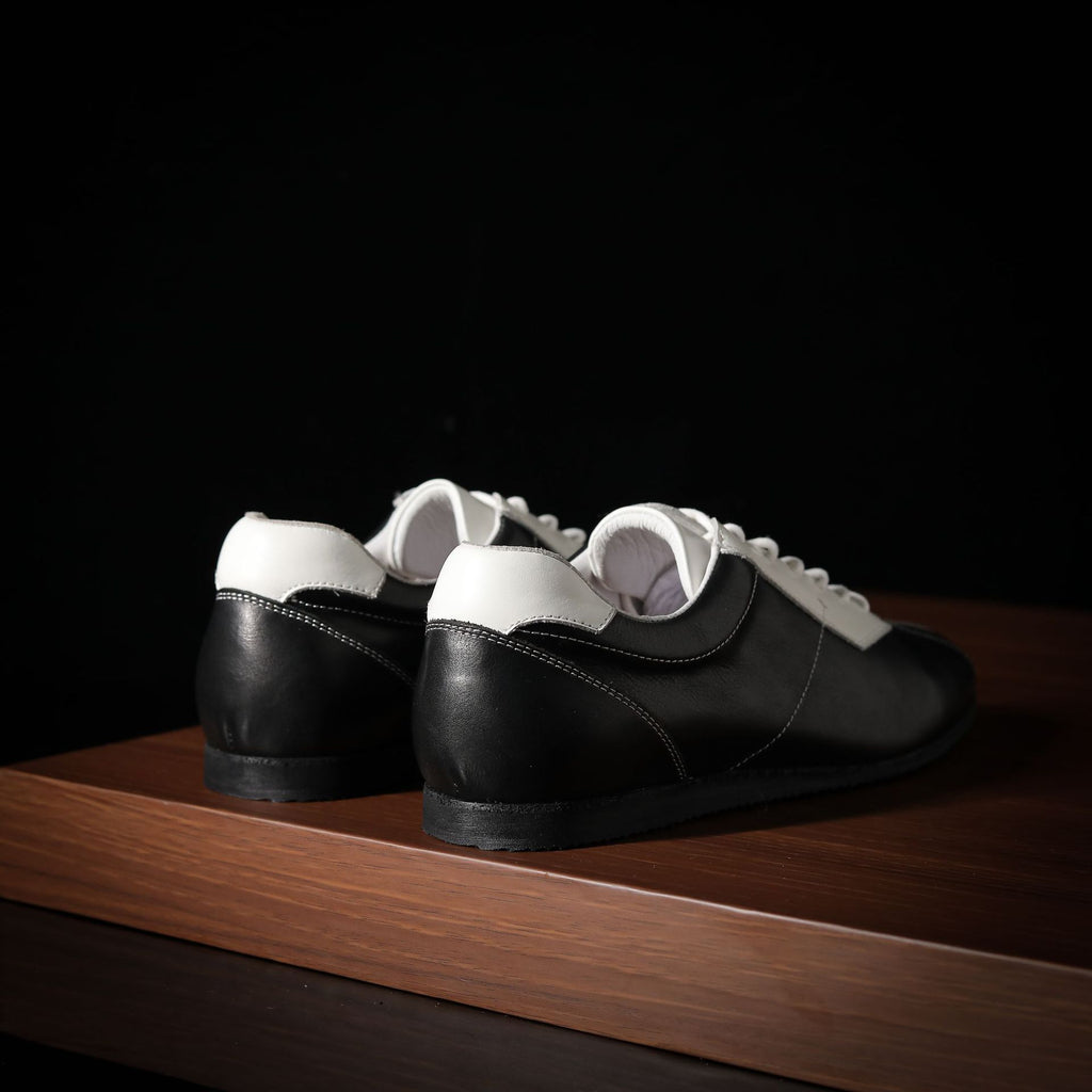 Black and white leather sneakers, rear view showing heel and collar contours.