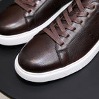 Close-up of dark brown leather sneakers with lace-up front and white rubber sole