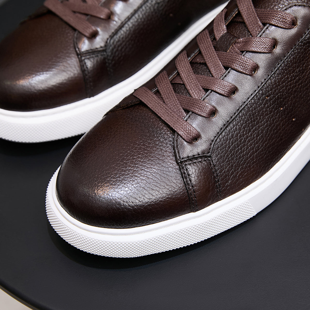 Close-up of dark brown leather sneakers with lace-up front and white rubber sole