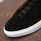 Men's black suede sneaker close-up with lace-up panel and white rubber sole