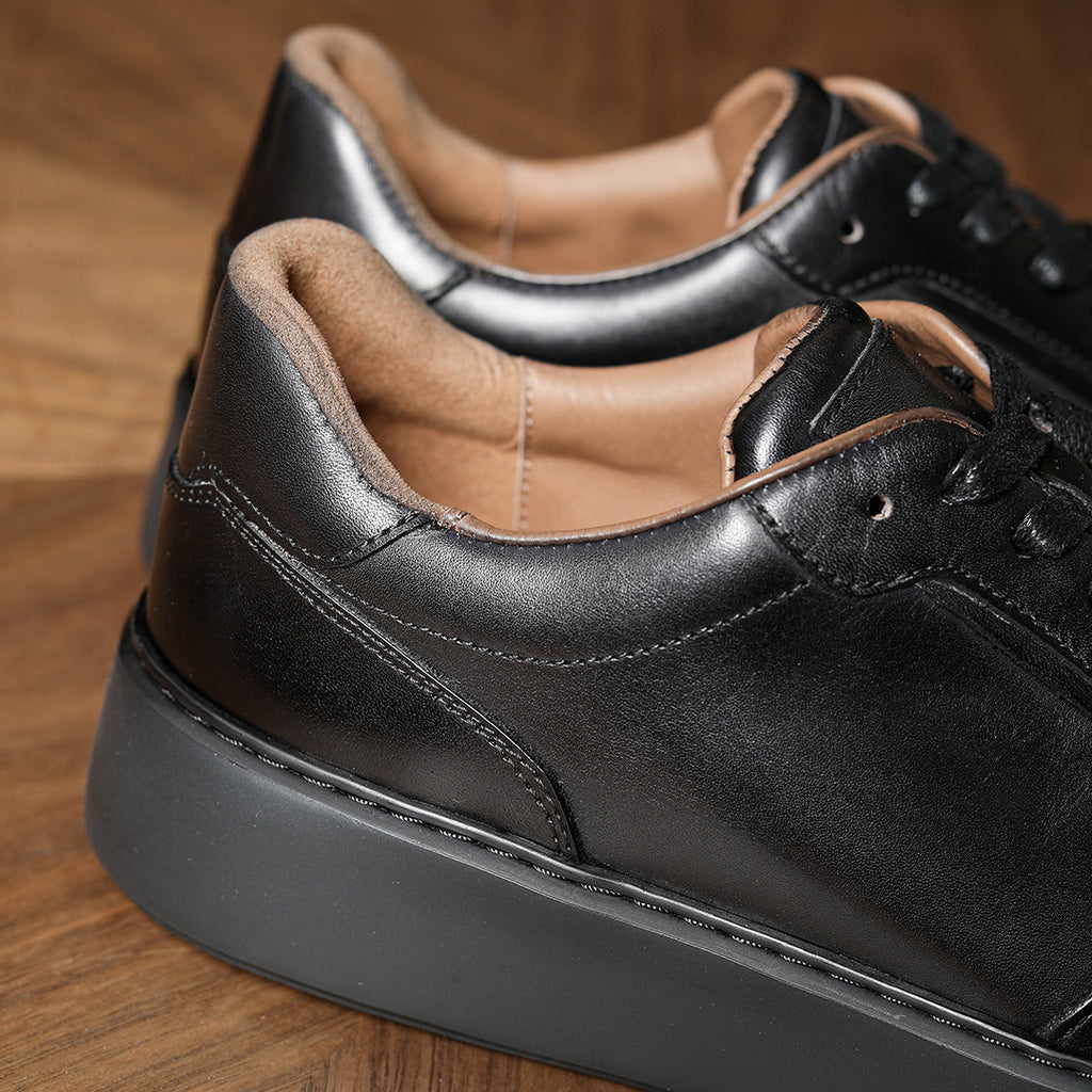 Black leather sneakers for men with padded collar, stitched details, and lace-up front.