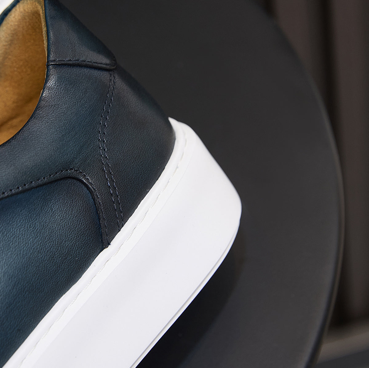 Dark blue leather sneaker side and heel with white midsole, lace-up collar detail.