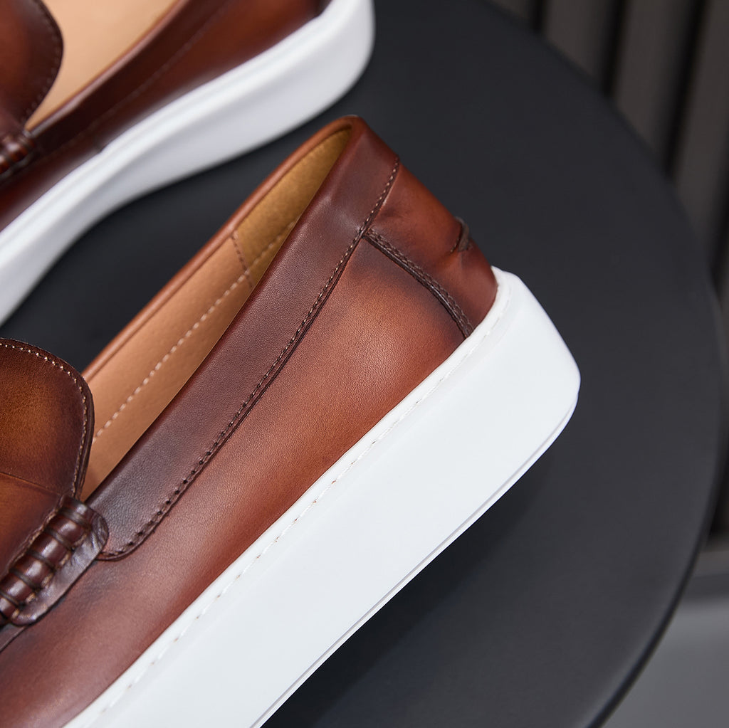 Men's brown leather slip-on sneaker side view with white sole and stitched seam panel.
