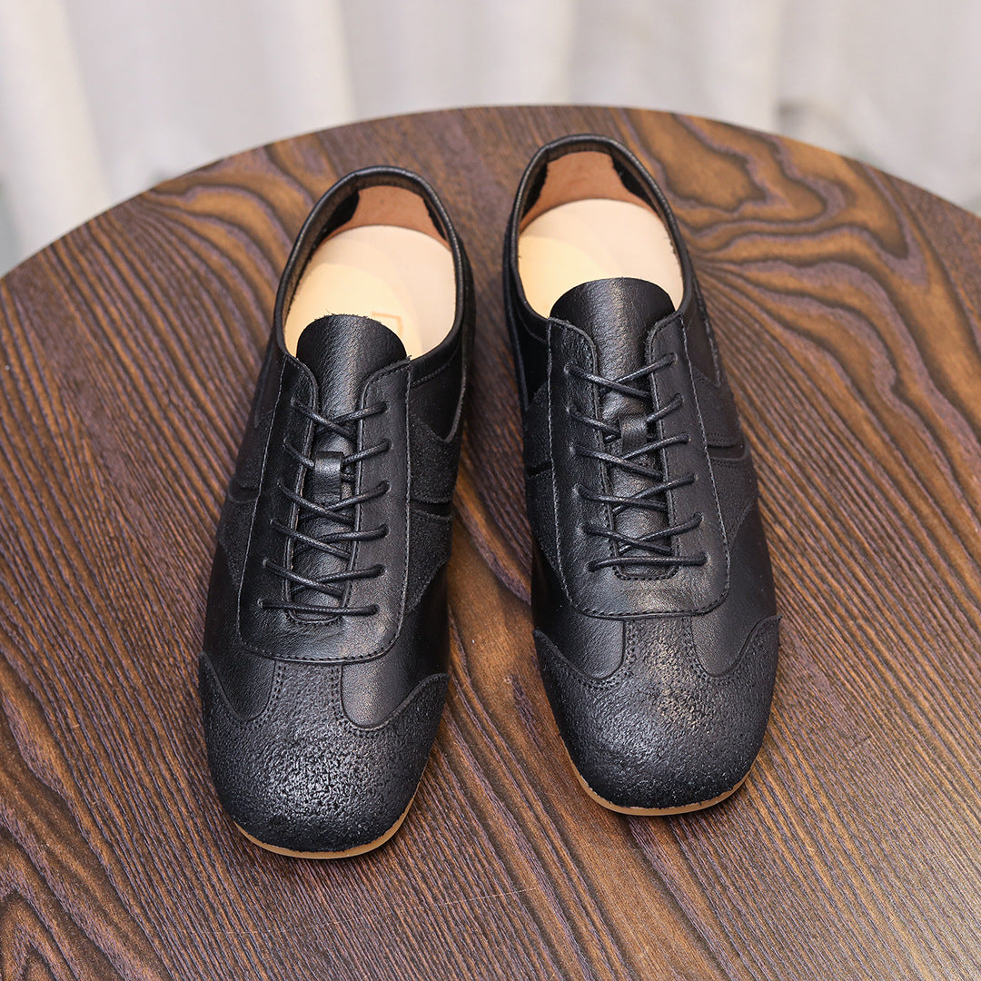 Men's black leather sneakers with laces and side panels, on a wooden surface