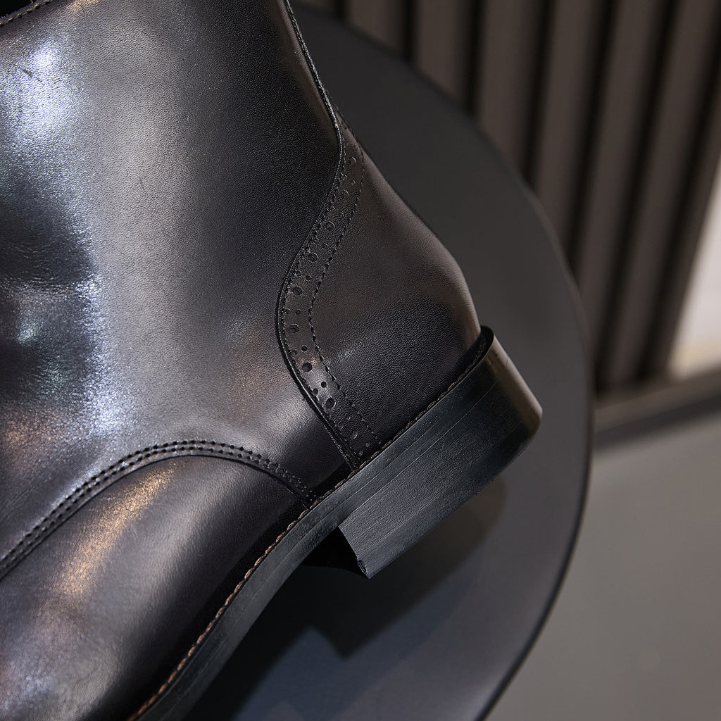 Black leather pointed-toe boot side view, stitched paneling and low stacked heel