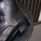Black leather pointed-toe boot side view, stitched paneling and low stacked heel