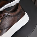 Men's dark brown leather sneaker close-up of textured upper, seam lines, and lace area