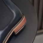 Side view detail of dark blue Chelsea dress boots with elastic panel and tan sole edge