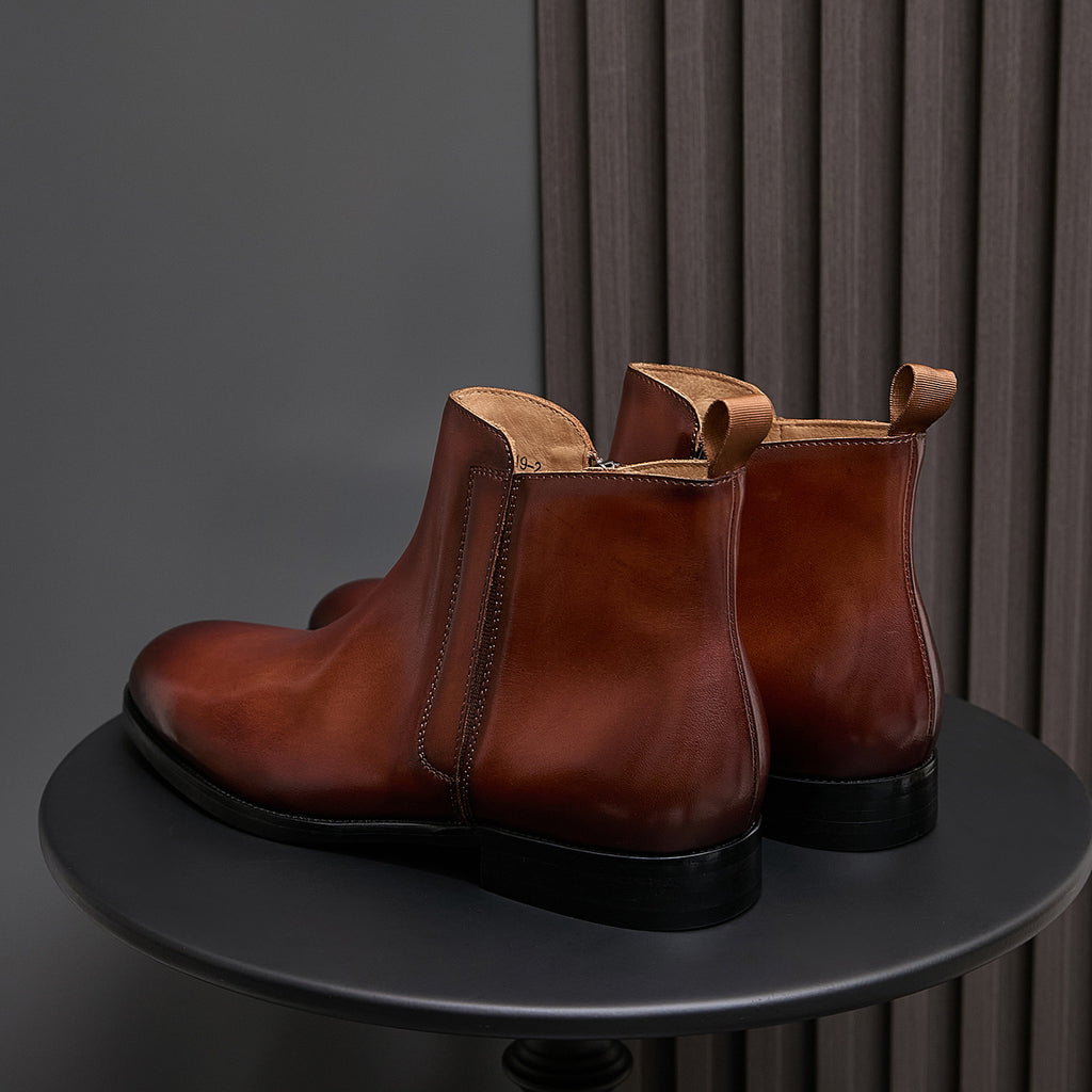 Pair of men's pointed-toe leather dress boots with side zip, brown leather and black sole.