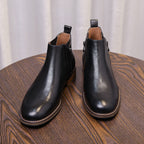 Black leather pointed-toe side-zip ankle boots pair, side angle on table.