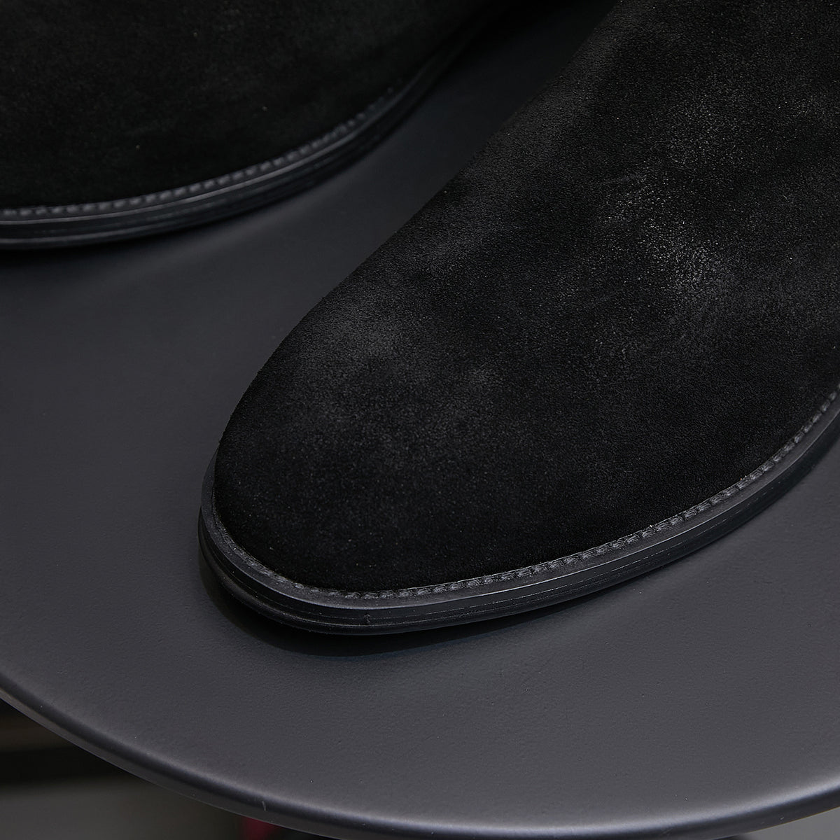 Close-up of black suede pointed toe Chelsea boot with dark rubber sole edge