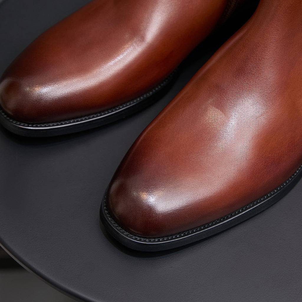 Close-up of men's brown pointed-toe leather dress boots with stitched sole edge.