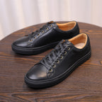 Black leather low-top sneakers with lace-up front and tan lining inside.