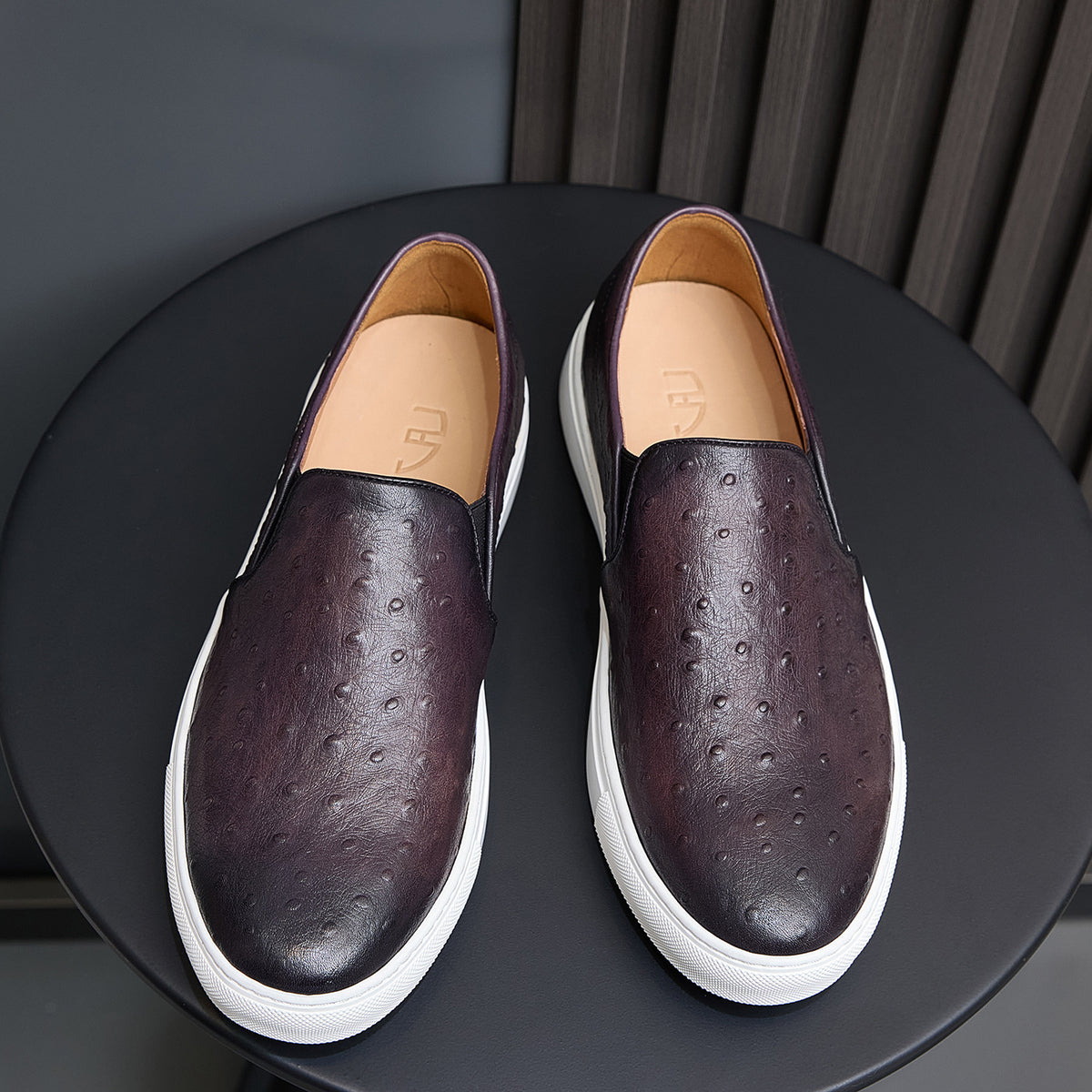 Pair of dark purple leather slip-on sneakers with perforations, tan lining, white sole