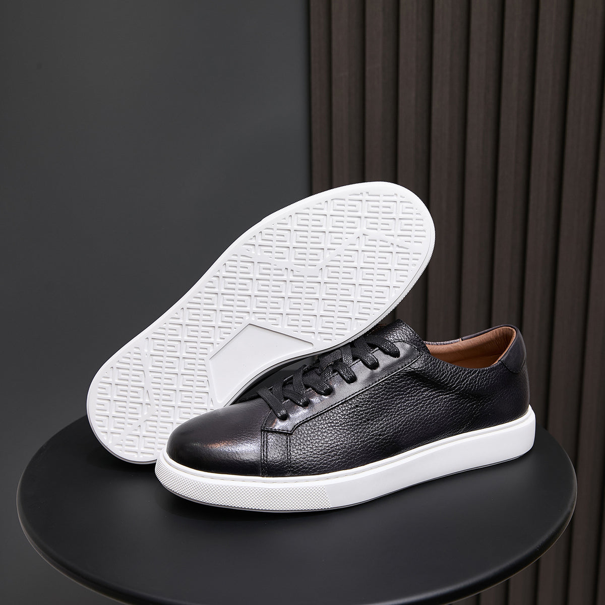 Black leather sneaker showing white outsole tread and lace-up upper