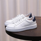 White genuine leather sneakers with lace-up front and dark blue heel accents.