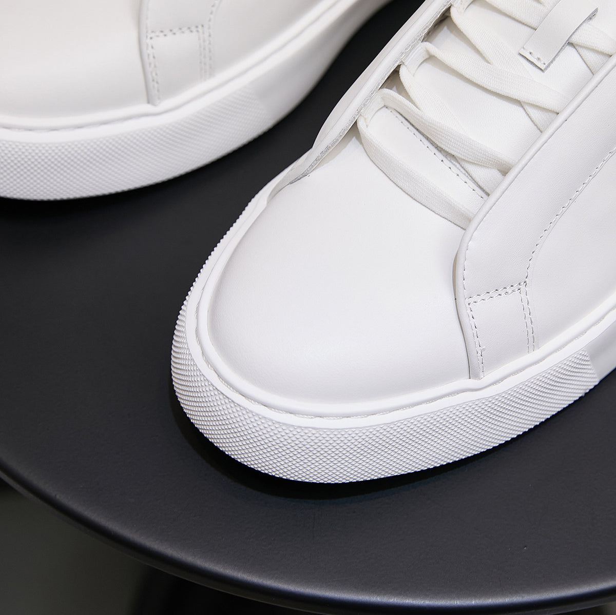 White leather low-top sneakers, close-up of laces and side stitching on rubber sole