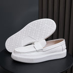 Men's white leather slip-on sneakers showing treaded outsole and moc toe upper.