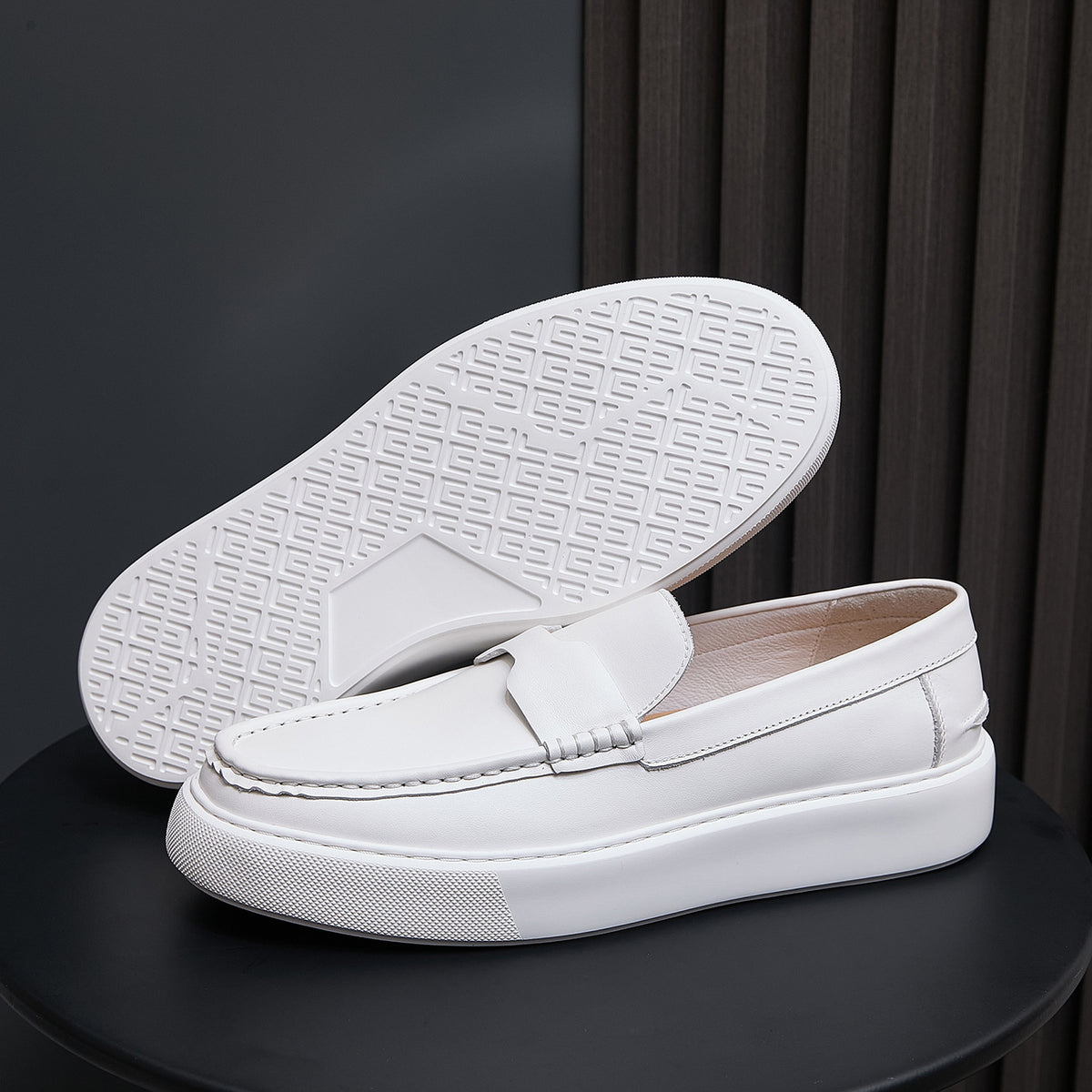 Men's white leather slip-on sneakers showing treaded outsole and moc toe upper.
