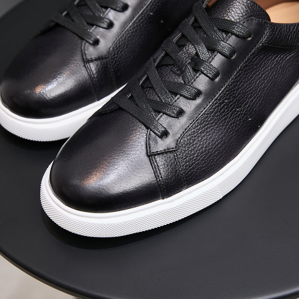 Black leather lace-up sneakers close-up with textured upper and white midsole