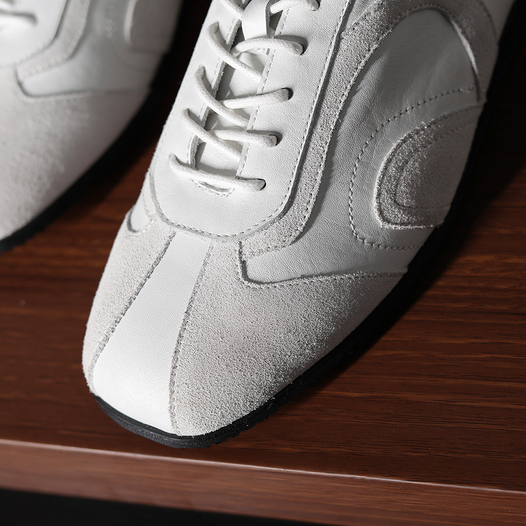 Close-up of white leather sneaker upper with lace-up eyelets and stitched side panel.